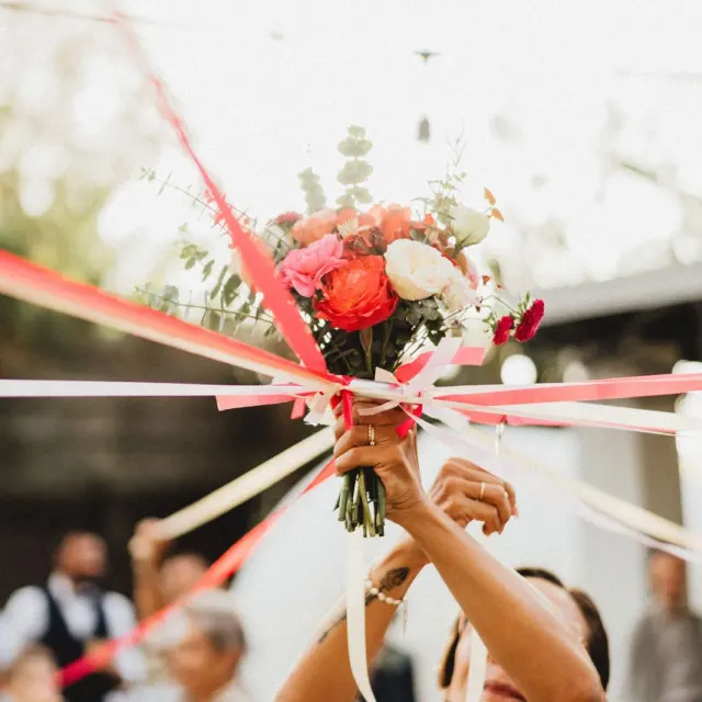 Lancer du bouquet de la mariée, orné de rubans rouges, pendant la réception
