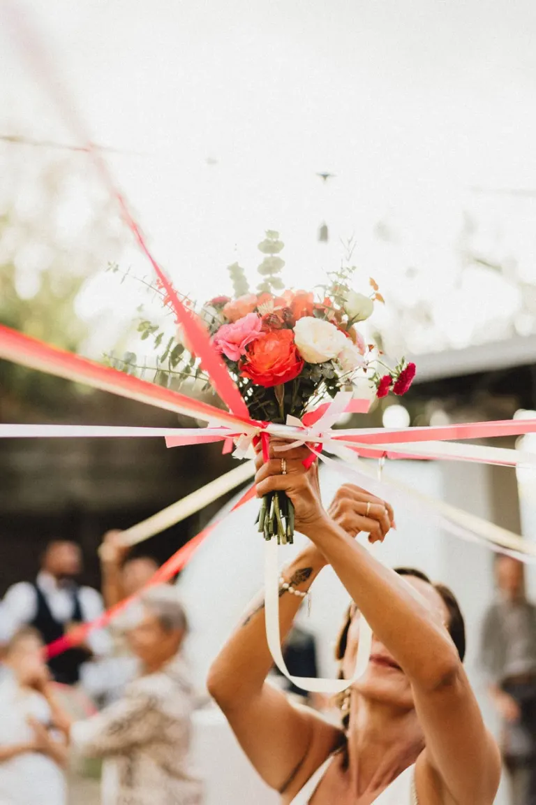 Lancer du bouquet de la mariée, orné de rubans rouges, pendant la réception
