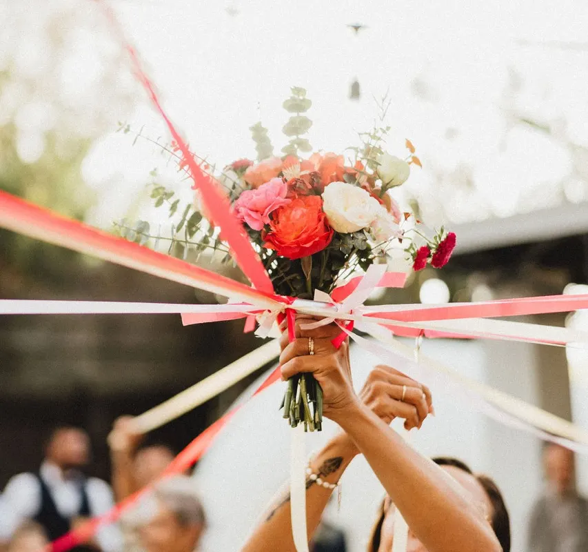 Lancer du bouquet de la mariée, orné de rubans rouges, pendant la réception