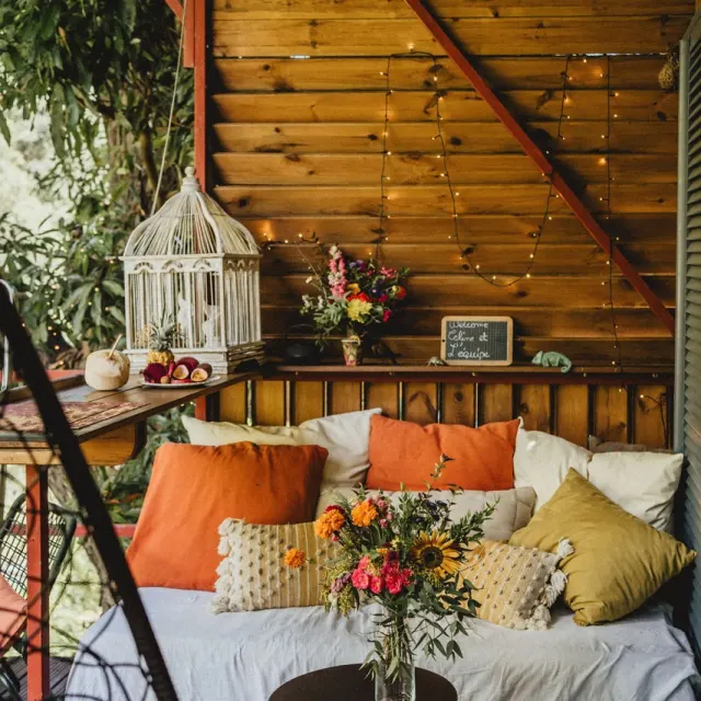 Coin salon cosy avec coussins colorés et fleurs, installé dans une case en bois