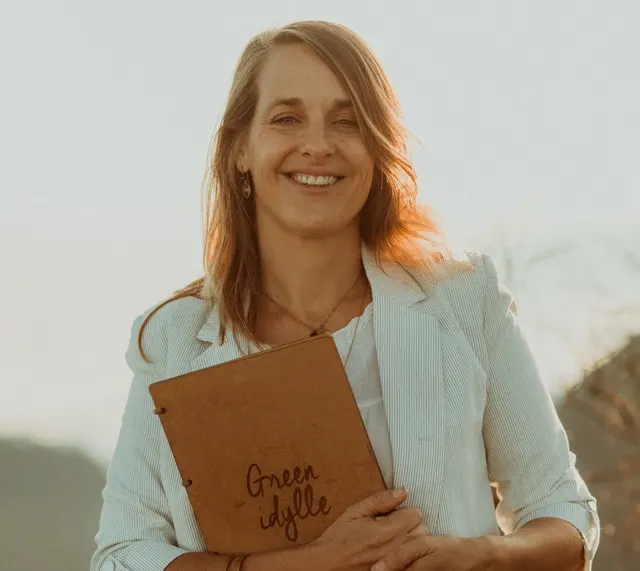 Céline, fondatrice de Green idylle, souriante avec son carnet en main dans une lumière dorée