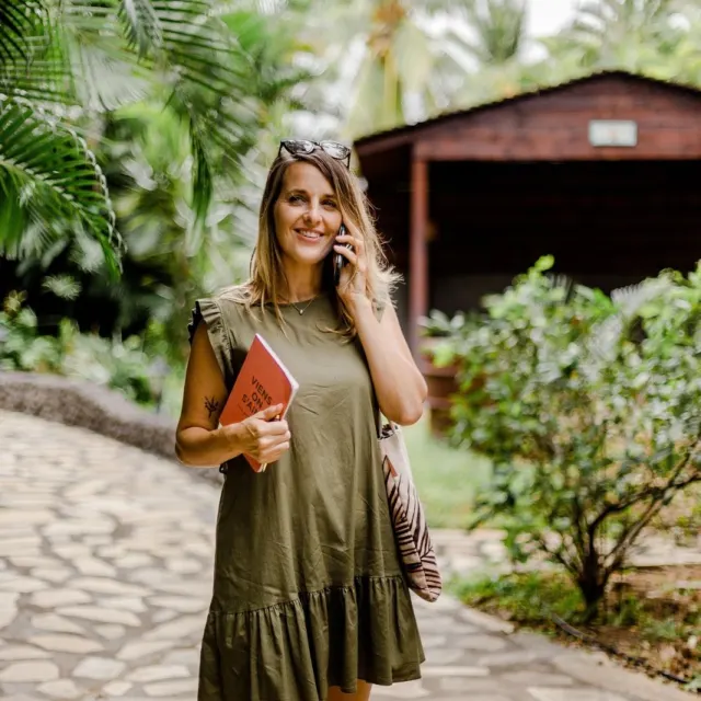 Céline au téléphone dans une allée tropicale bordée de fleurs colorées