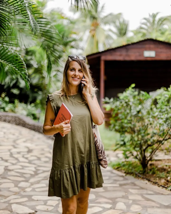 Céline au téléphone dans une allée tropicale bordée de fleurs colorées