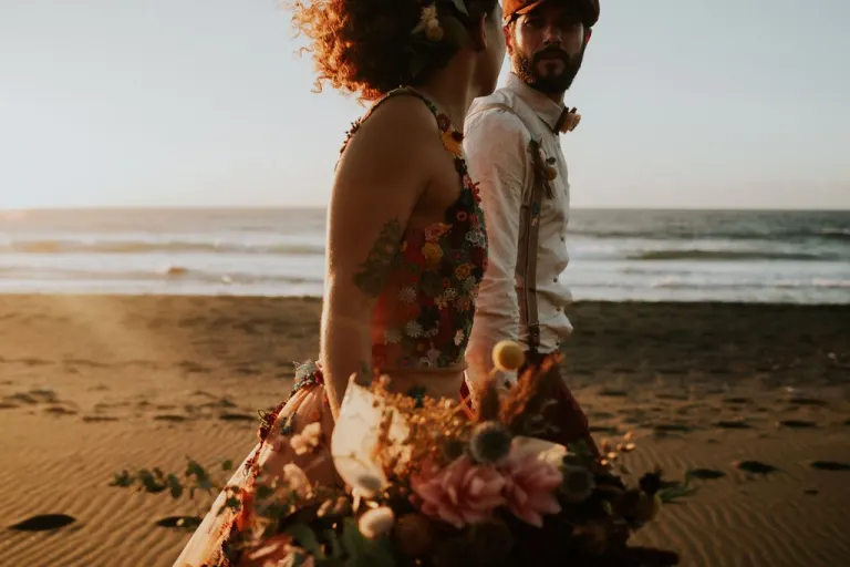 Mariés sur la plage, la mariée en robe fleurie avec des fleurs à la main