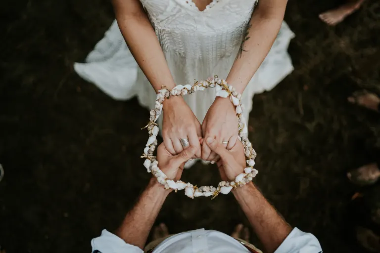 Deux mains tenant une couronne de fleurs fraîches lors d’un mariage en extérieur