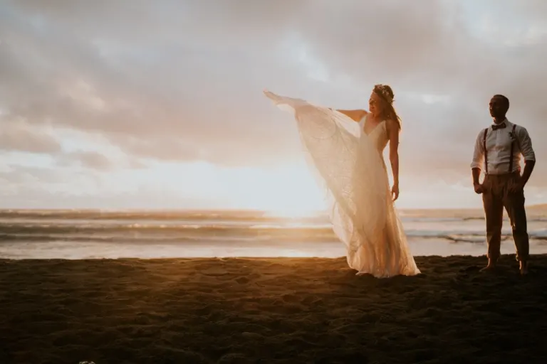 Couple de mariés au coucher du soleil sur une plage de sable noir