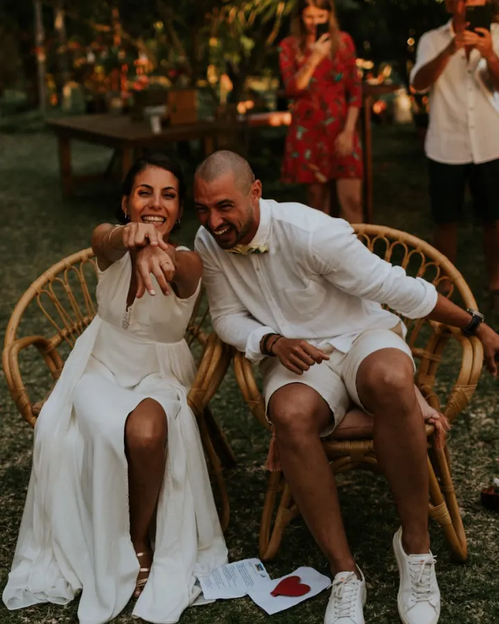 Jeunes mariés rieurs installés dans des fauteuils en rotin pendant leur mariage