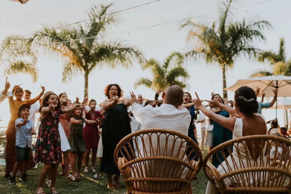 Mariés et invités sous les palmiers, installés dans des fauteuils en rotin pendant la réception