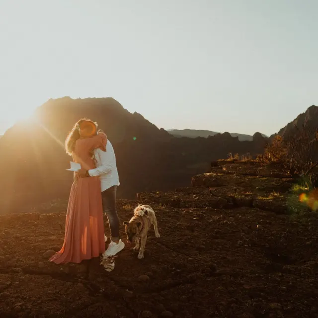 Couple de jeunes mariés et leur chien sur un paysage volcanique au soleil couchant
