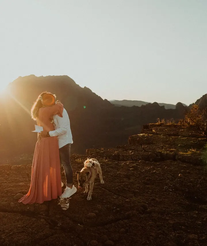 Couple de jeunes mariés et leur chien sur un paysage volcanique au soleil couchant