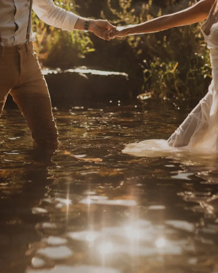 Jeunes mariés debout dans l’eau d’une rivière, entourés d’un décor sauvage et verdoyant