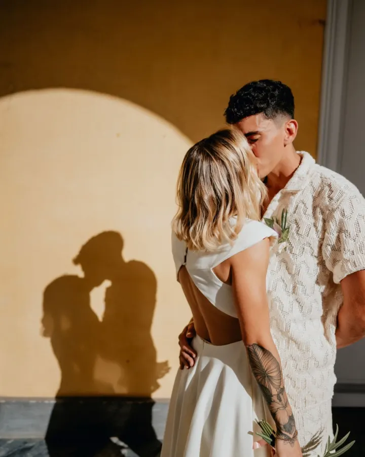 Mariés enlacés sous une arche de cérémonie, dans un jeu d’ombres et de lumière