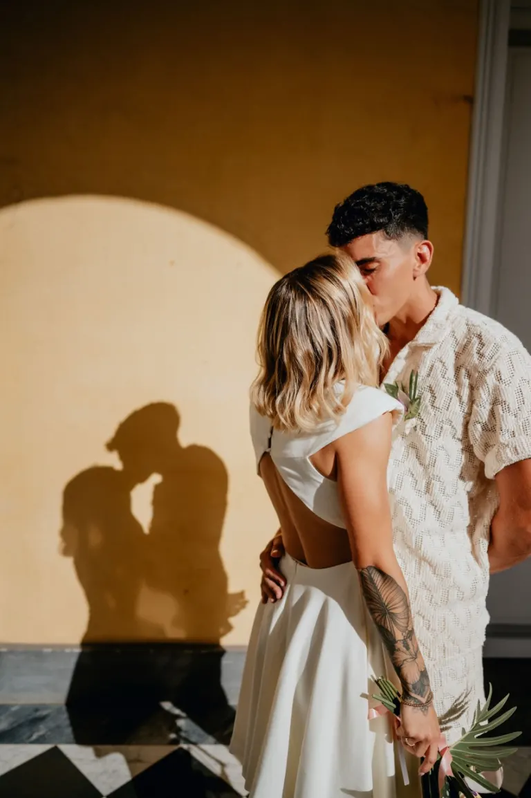 Mariés enlacés sous une arche de cérémonie, dans un jeu d’ombres et de lumière