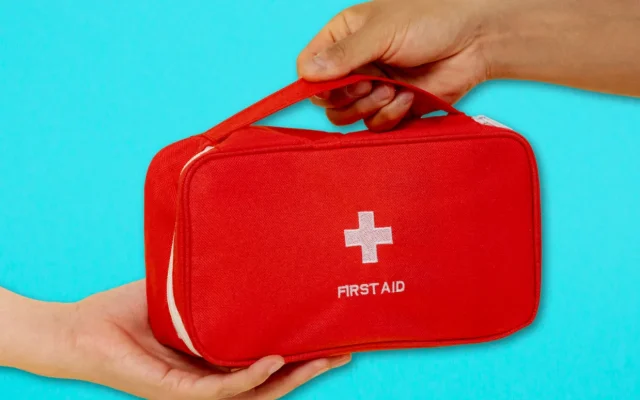 Deux mains se transmettent une trousse de premiers secours rouge sur fond turquoise.