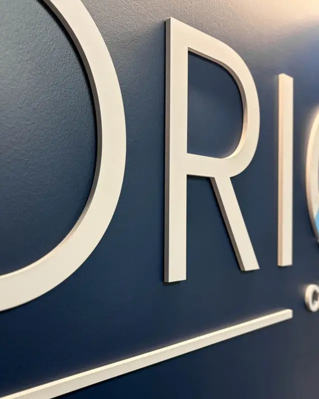 Lettres blanches en relief du nom Orion et logo coloré sur un mur bleu marine