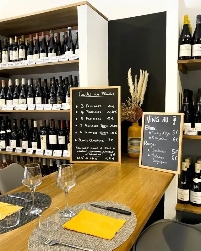 Table haute en bois devant les ardoises de la carte des planches et des vins au verre et des étagères de bouteilles