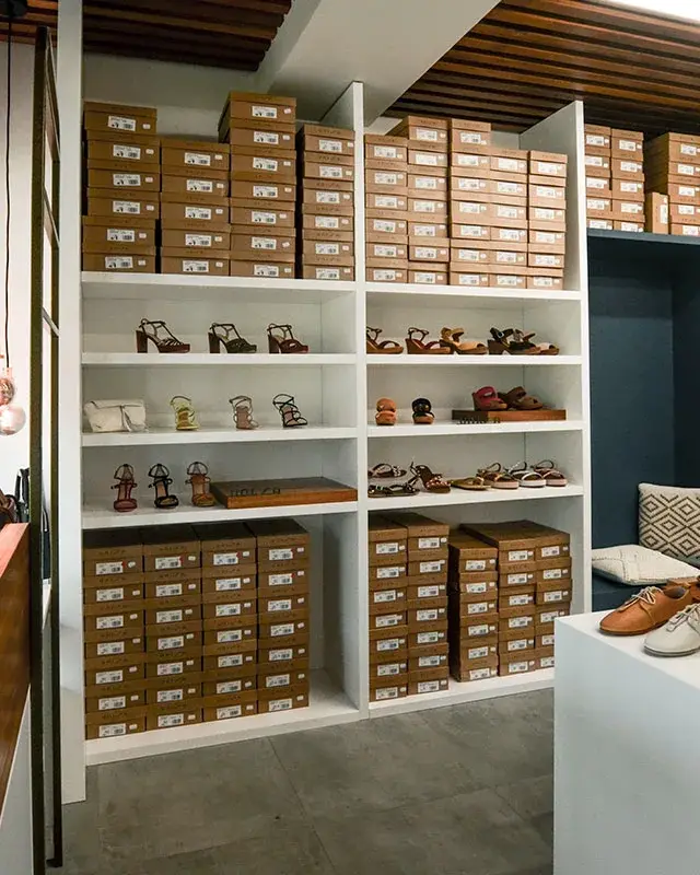 Boutique Chaus’en Folie à L’Ermitage-les-Bains agencée par Décogité : étagères blanches, plateaux en bois, niche bleu nuit et vitrine éclairée par des suspensions