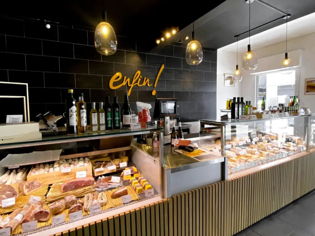 Comptoir réfrigéré habillé de tasseaux de bois devant un mur noir au logo doré, dans la boutique Enfin ! Le Fromager à Saint-Denis