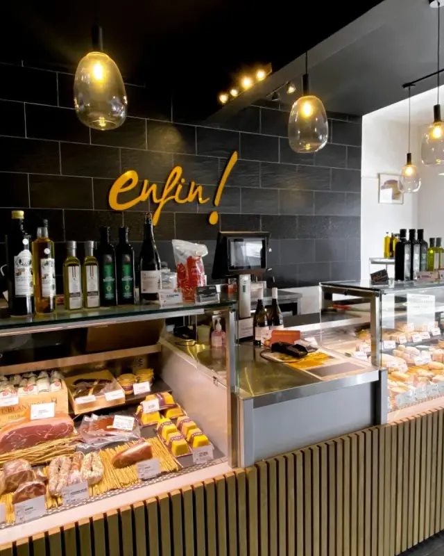 Comptoir en L réunissant vitrines de charcuterie et de fromages, caisse et épicerie fine, sur fond noir