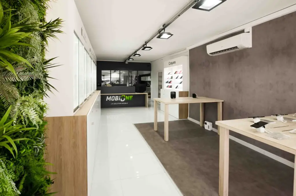 Allée de la boutique MobiOne à Saint-Paul, entre mur végétal, vitrines murales éclairées et tables de démonstration en bois clair