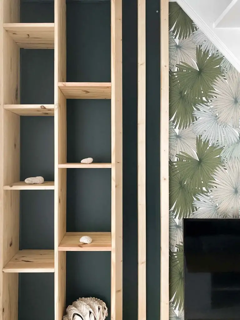 Bibliothèque sur mesure en bois clair et papier peint à feuilles tropicales dans un T4 aménagé à Saint-Leu
