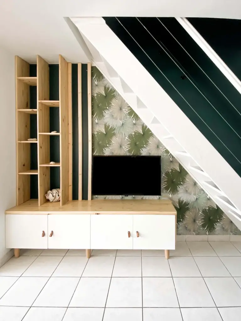 Meuble sur mesure en pin et blanc sous l’escalier, papier peint palmiers et cage d’escalier vert sapin dans un T4 à Saint-Leu