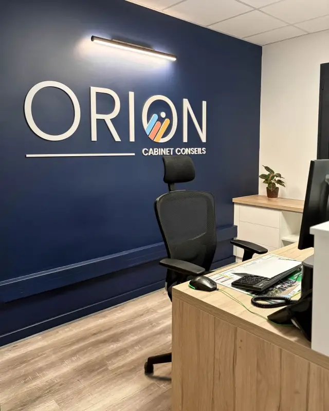 Accueil du cabinet comptable Orion à Saint-Joseph : mur bleu nuit, logo lumineux et bureau en bois