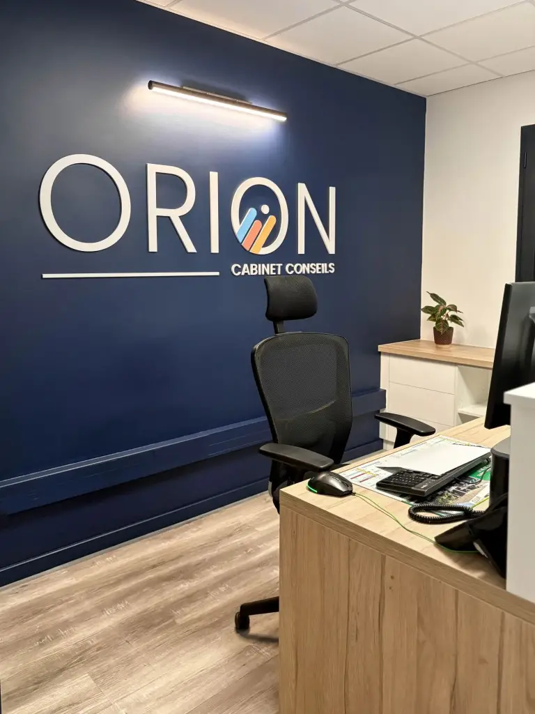 Accueil du cabinet comptable Orion à Saint-Joseph avec mur bleu marine, lettres blanches en relief et banque d’accueil en décor chêne