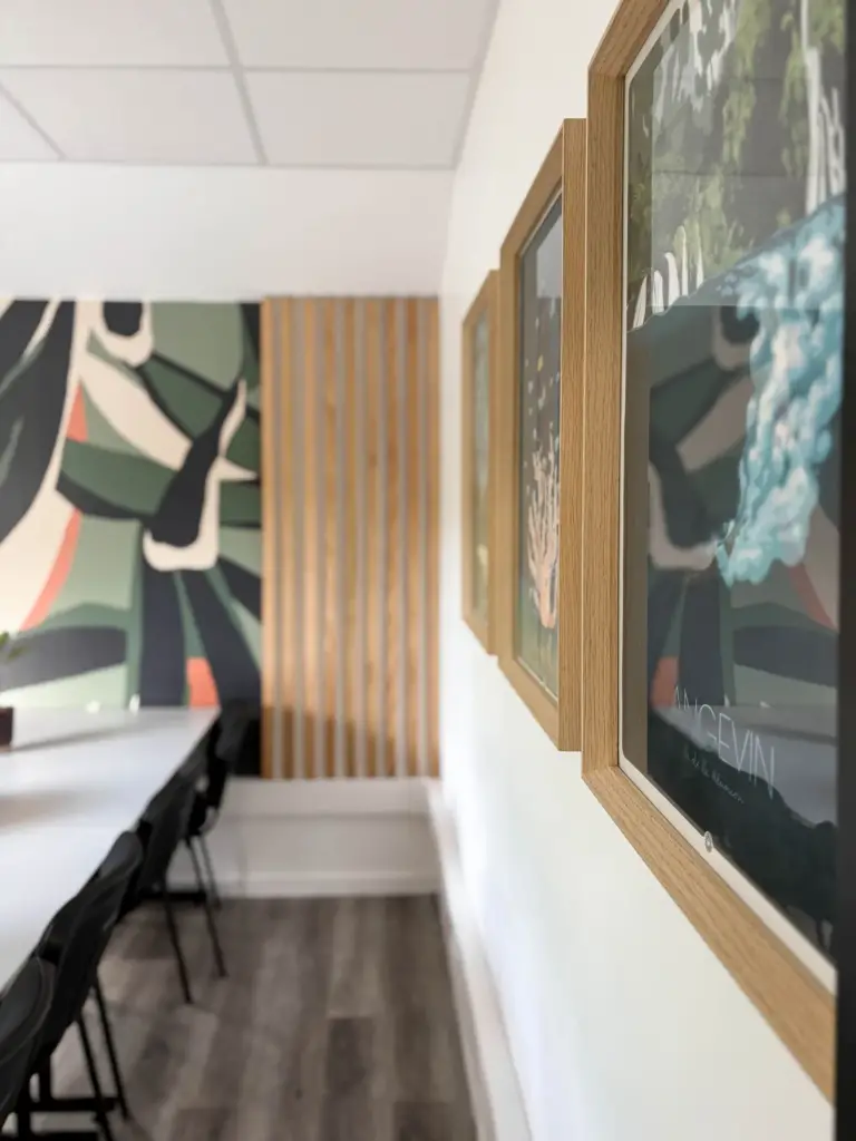 Rangée de postes de travail le long d’un mur de papier peint tropical, avec cadres décoratifs et claustra en bois, au cabinet Orion à Saint-Joseph