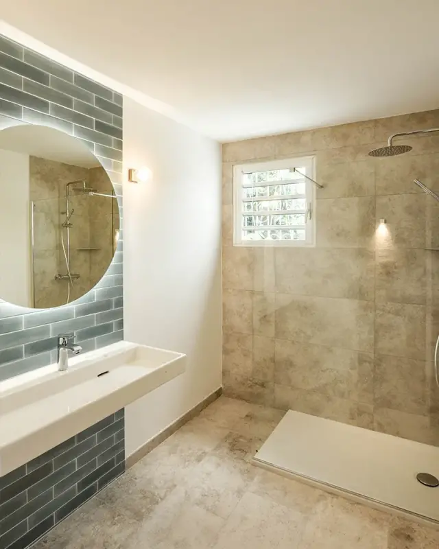 Salle de bains d’une maison à Saint-Paul avec faïence bleu-gris, miroir rond rétroéclairé et douche vitrée