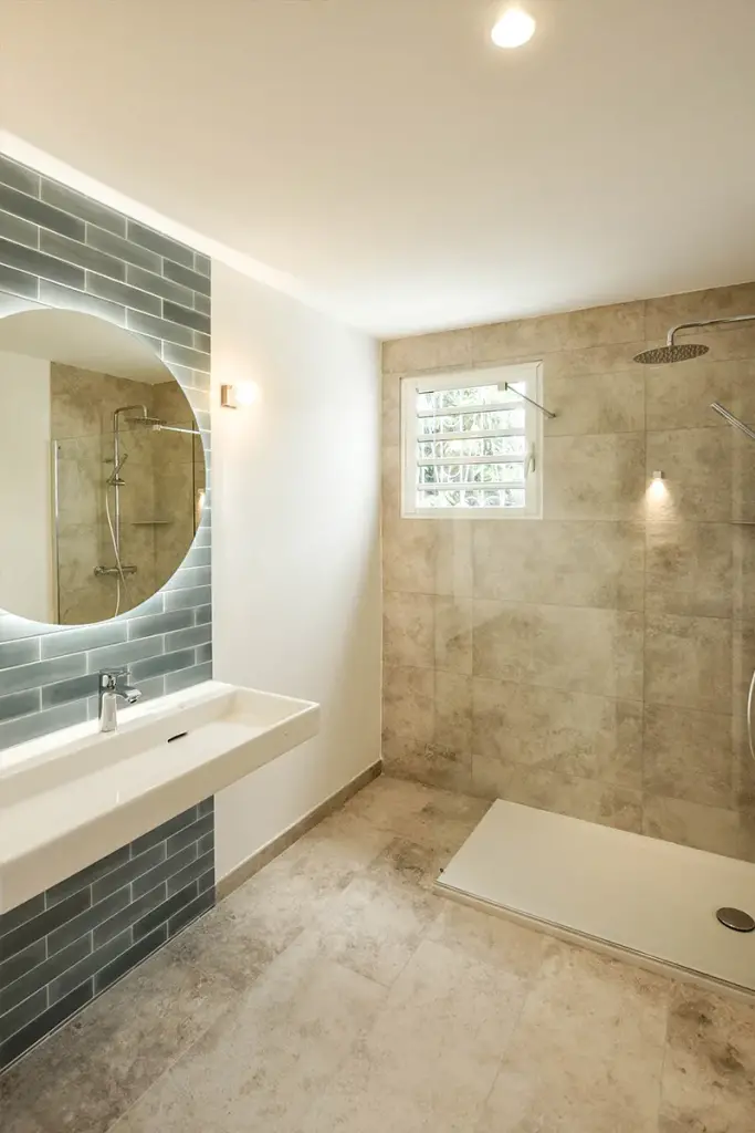 Salle de bains d’une maison à Saint-Paul avec faïence bleu-gris, miroir rond rétroéclairé et douche vitrée