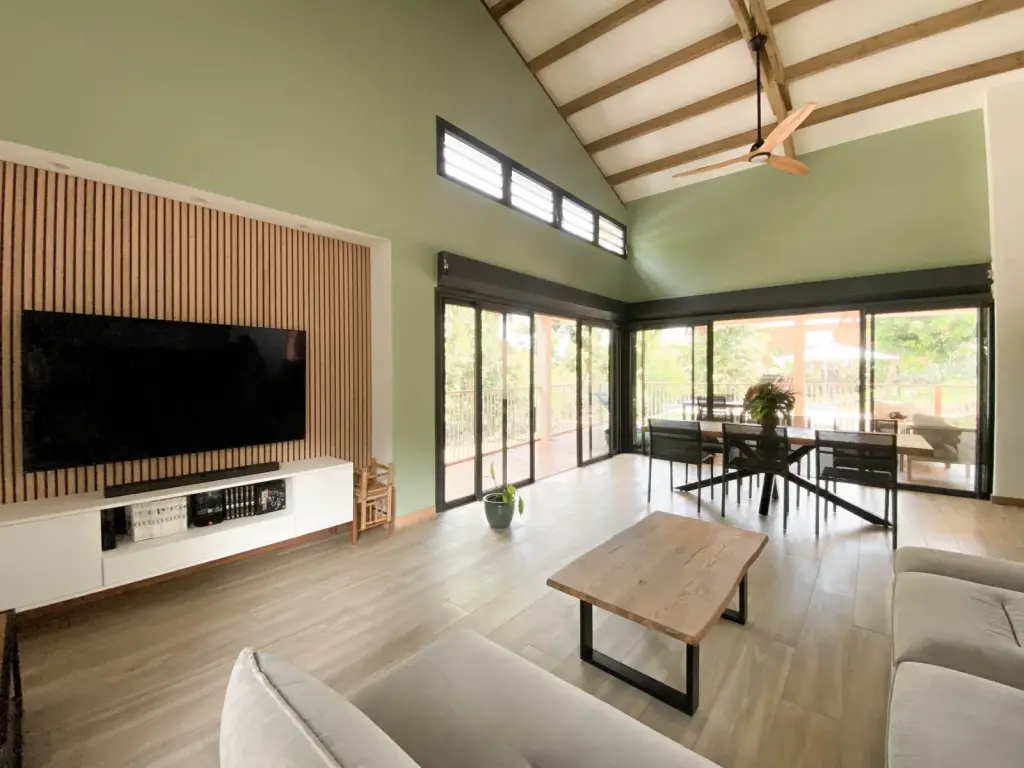 Pièce de vie d’une maison neuve à L’Étang-Salé avec mur vert sauge, charpente apparente et panneau de tasseaux en bois