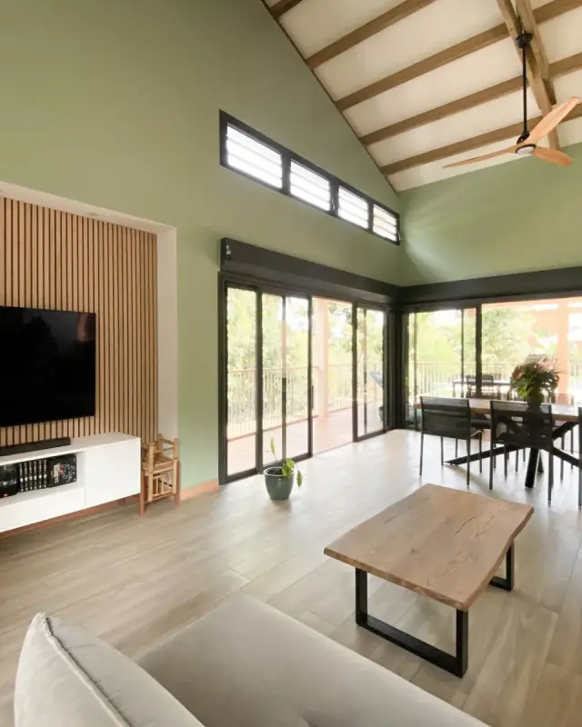 Pièce de vie d’une maison neuve à L’Étang-Salé avec mur vert sauge, charpente apparente et panneau de tasseaux en bois