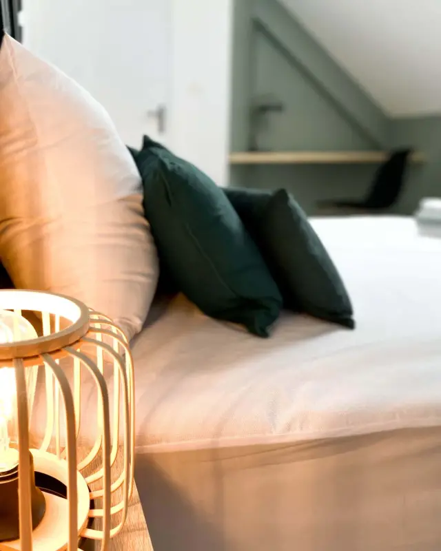 Chambre blanche avec lampe cage en bambou, coussins vert sapin et coin bureau vert sauge sous la pente