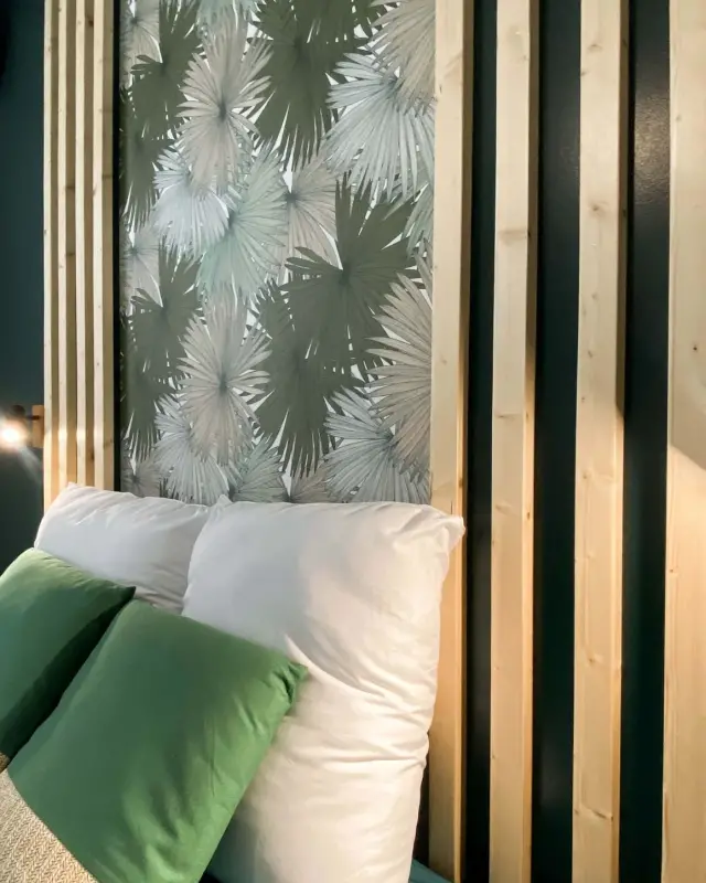 Tête de lit en tasseaux de pin encadrant un lé de papier peint palmiers sur fond vert foncé