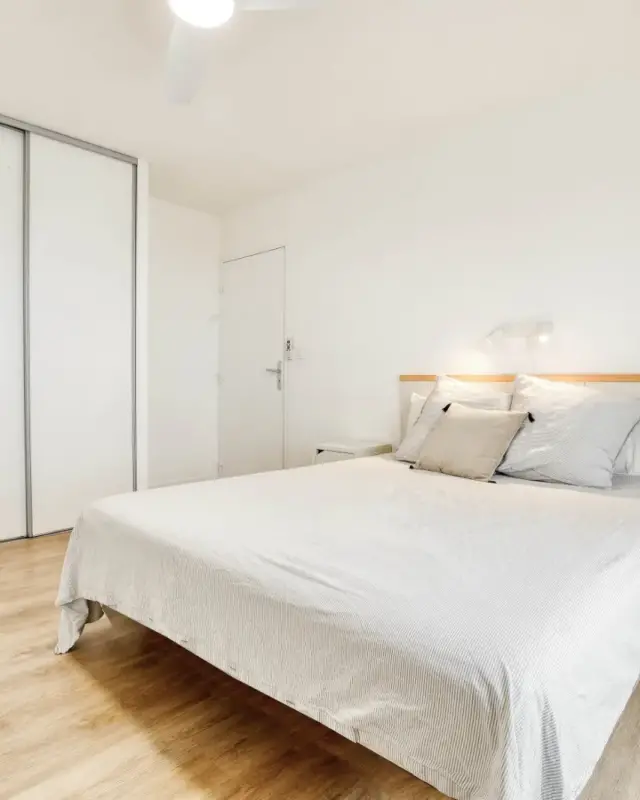 Chambre blanche avec placard coulissant, tête de lit blanc et bois et sol stratifié chêne clair