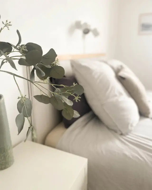 Branche d’eucalyptus dans un vase vert près d’un lit au linge rayé