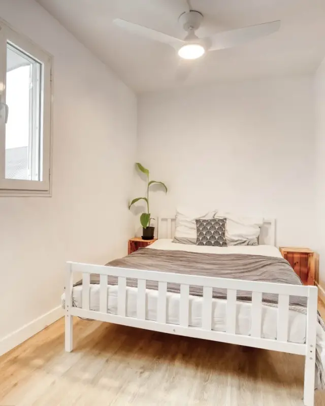 Petite chambre avec lit en bois blanc, caisses en bois en guise de chevets et guitare au mur
