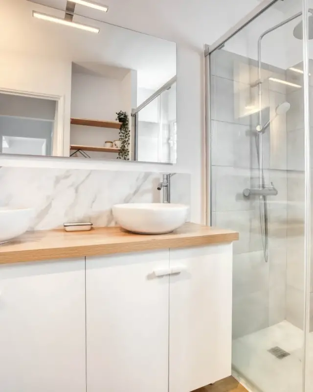 Salle d’eau avec meuble double vasque au plan effet chêne, crédence effet marbre et douche vitrée