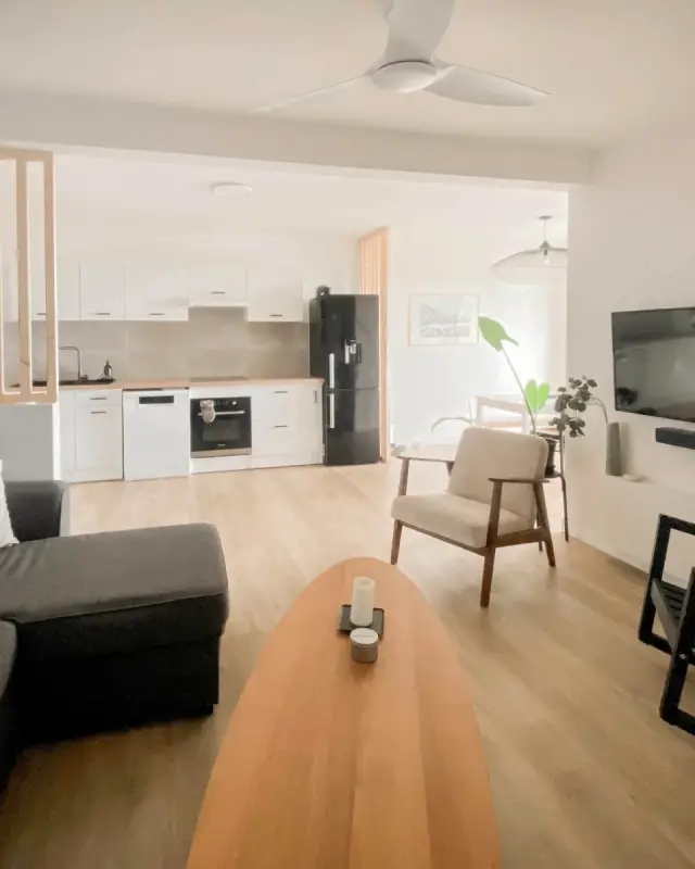Salon avec canapé d’angle anthracite, table basse ovale en bois et ventilateur de plafond blanc