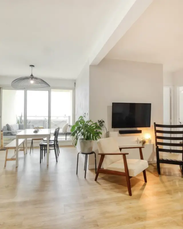Séjour lumineux avec coin repas devant la baie, fauteuil en bois, rocking-chair noir et claustra en pin