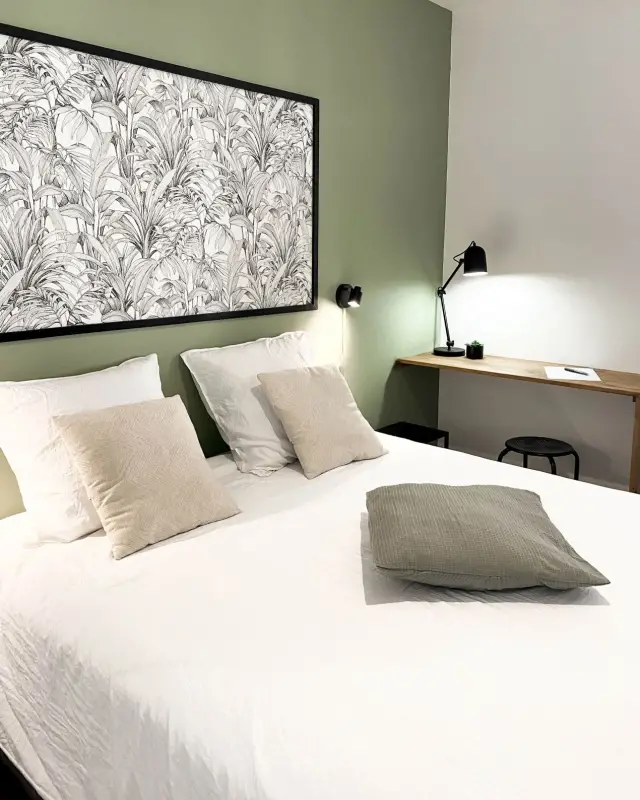 Chambre au mur vert sauge avec papier peint feuillage encadré de noir, liseuse et bureau en tablette de bois