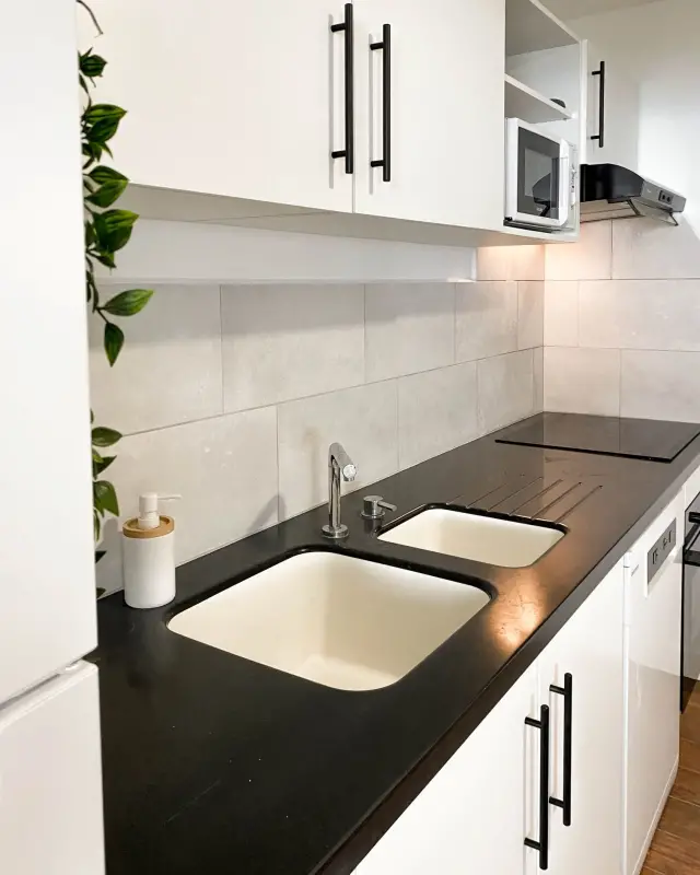 Cuisine blanche aux poignées noires, plan de travail noir, double évier et crédence gris clair