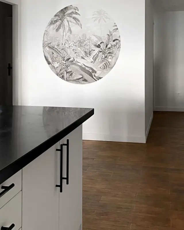 Médaillon rond de papier peint jungle en noir et blanc face à une cuisine au plan de travail noir