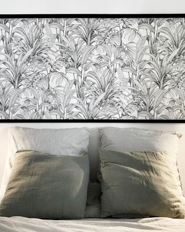 Tête de lit en papier peint feuillage noir et blanc encadré, deux liseuses noires et coussins vert sauge