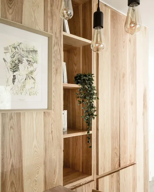 Rangements toute hauteur en bois clair avec niches ouvertes, affiche botanique et ampoules suspendues