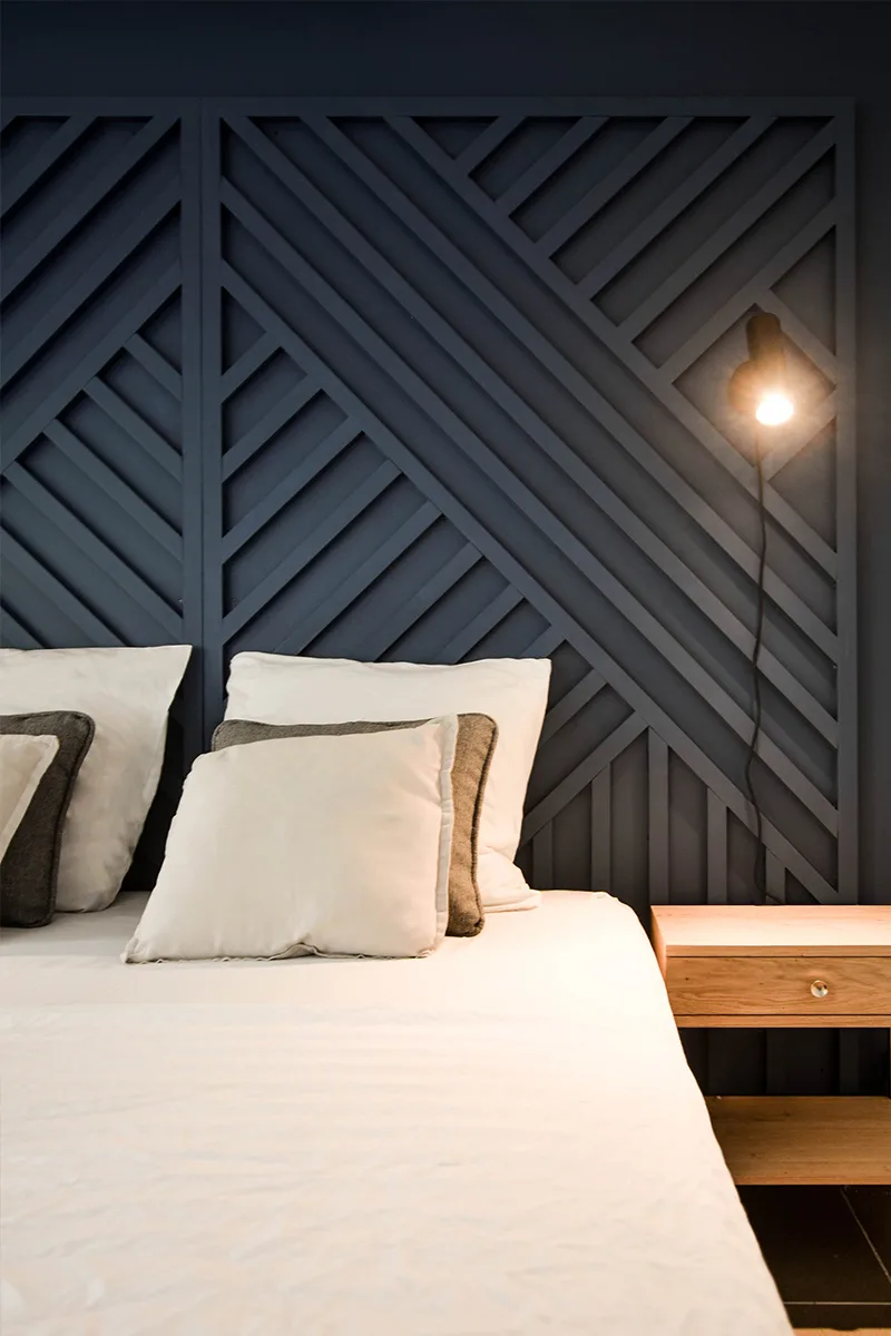 Chambre d’une location saisonnière à Saint-Gilles-les-Bains avec tête de lit en panneau de bois bleu nuit et linge blanc
