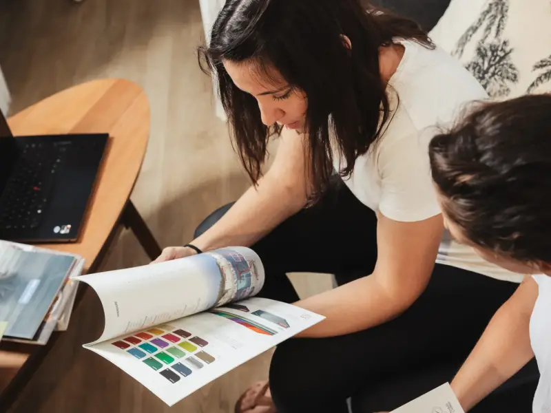 Hermine et Amanda feuillettent un magazine de décoration et un nuancier de couleurs à l’agence Décogité