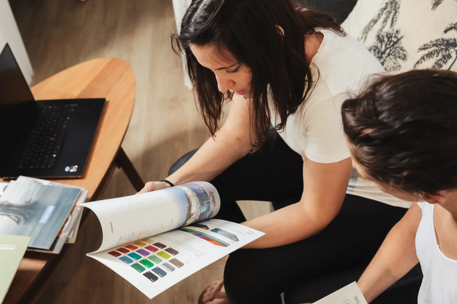 Hermine et Amanda feuillettent un magazine de décoration et un nuancier de couleurs à l’agence Décogité