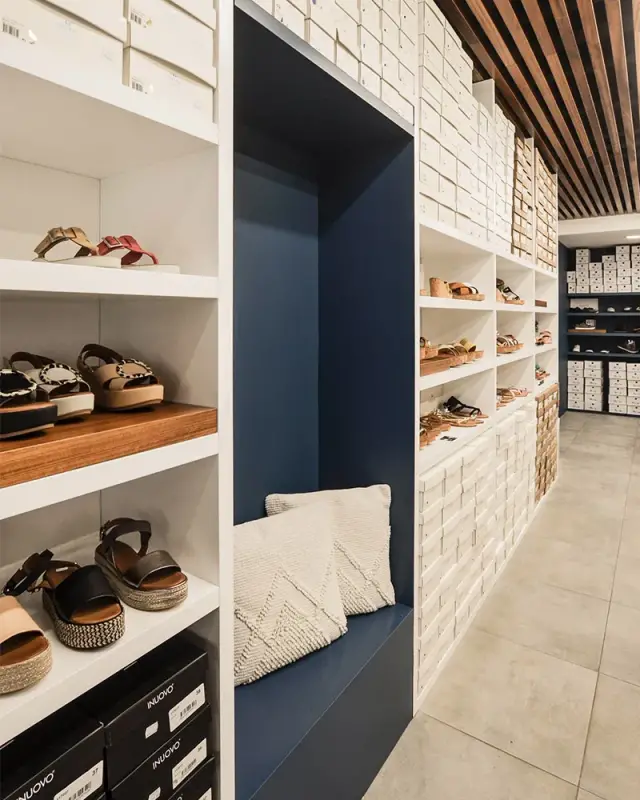 Banquette d’essayage dans une niche bleu marine entre des rayonnages blancs de chaussures et de boîtes